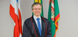 Pra todos verem: Homem de pele clara, cabelos grisalhos curtos e óculos, posando para foto ofici...