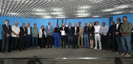 Foto 01: Fotografia de um grupo com cerca de 20 pessoas em pé, alinhadas lado a lado sobre um pa...