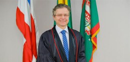 Pra todos verem: Homem de pele clara, cabelos grisalhos curtos e óculos, posando para foto ofici...
