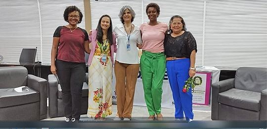 Pra Cego Ver: Foto de 5 mulheres levantadas, enfileiradas e abraçadas. O grupo se encontra no auditório do TRE-BA.