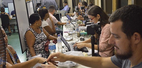 Foto de servidores fazendo atendimento a eleitores, coletando dados biométricos.