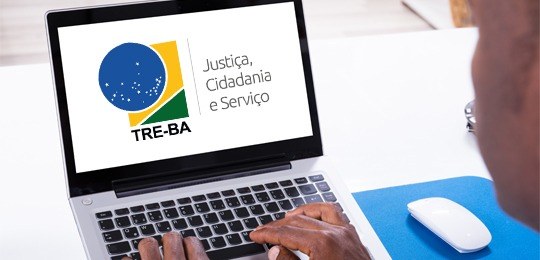 Uma pessoa diante de um notebook e dentro da tela a logomarca do TRE-BA e, à direita, seu slogan...