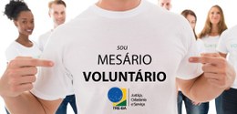 Uma pessoa com uma camisa com a inscrição "Sou mesário voluntário" e, logo abaixo, a logomarca d...